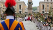 Swiss Guards and faithful pilgrims holding olive branches line the processional route in St. Peter’s Square for Palm Sunday celebrations, April 13, 2025. The ancient Vatican obelisk stands at the center of the square as clergy process toward the basilica.