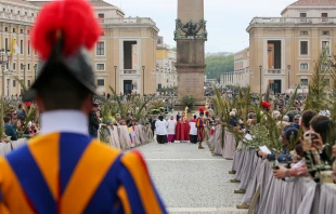 Swiss Guards and faithful pilgrims holding olive branches line the processional route in St. Peter’s Square for Palm Sunday celebrations, April 13, 2025. The ancient Vatican obelisk stands at the center of the square as clergy process toward the basilica. Credit: Bénédicte Cedergren/EWTN News