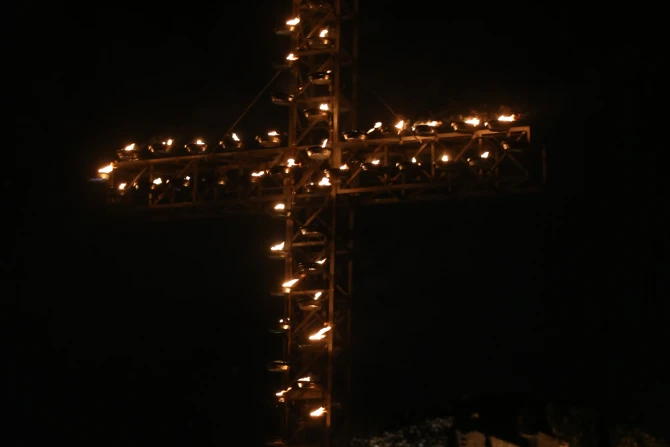 The illuminated cross stands against the night sky overlooking Rome's Colosseum