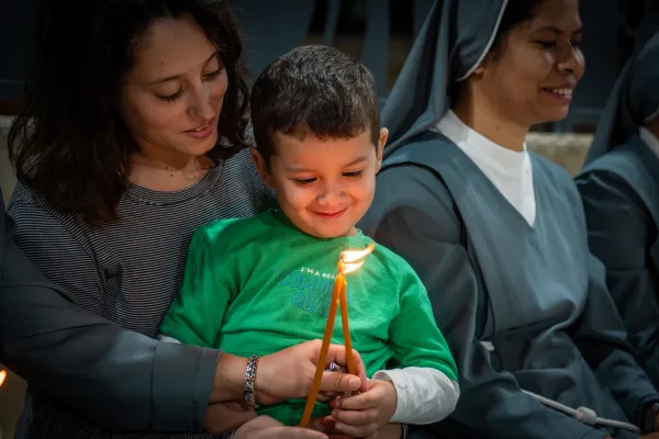 A child smiles in his mother's arms after lighting candles during the prayer vigil celebrated on Nov. 9, 2023, at the Terra Sancta High School in Jerusalem. Credit: Marinella Bandini