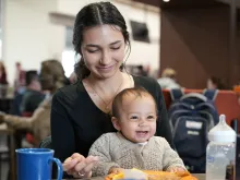 Katie Chihoski, a student at the University of Mary in Bismarck, North Dakota, eats with her baby, Lucia, on her lap in the company of fellow students. Chihoski is among the first students to benefit from a new initiative at the Catholic college called the Saint Teresa of Calcutta Community for Mothers, which provides free babysitting and other material support for young mothers on campus.