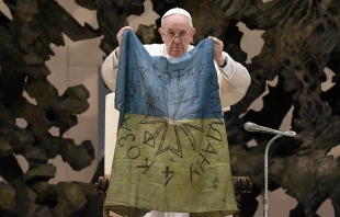 Pope Francis holds up a flag which he said was brought to him from “the martyred city” of Bucha, Ukraine at his general audience on April 6, 2022. Vatican Media