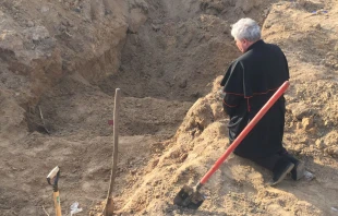 Papal envoy Cardinal Konrad Krajewski prays at a mass grave in Ukraine on Good Friday, April 15, 2022. Vatican Media.
