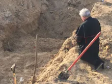Papal envoy Cardinal Konrad Krajewski prays at a mass grave in Ukraine on Good Friday, April 15, 2022.