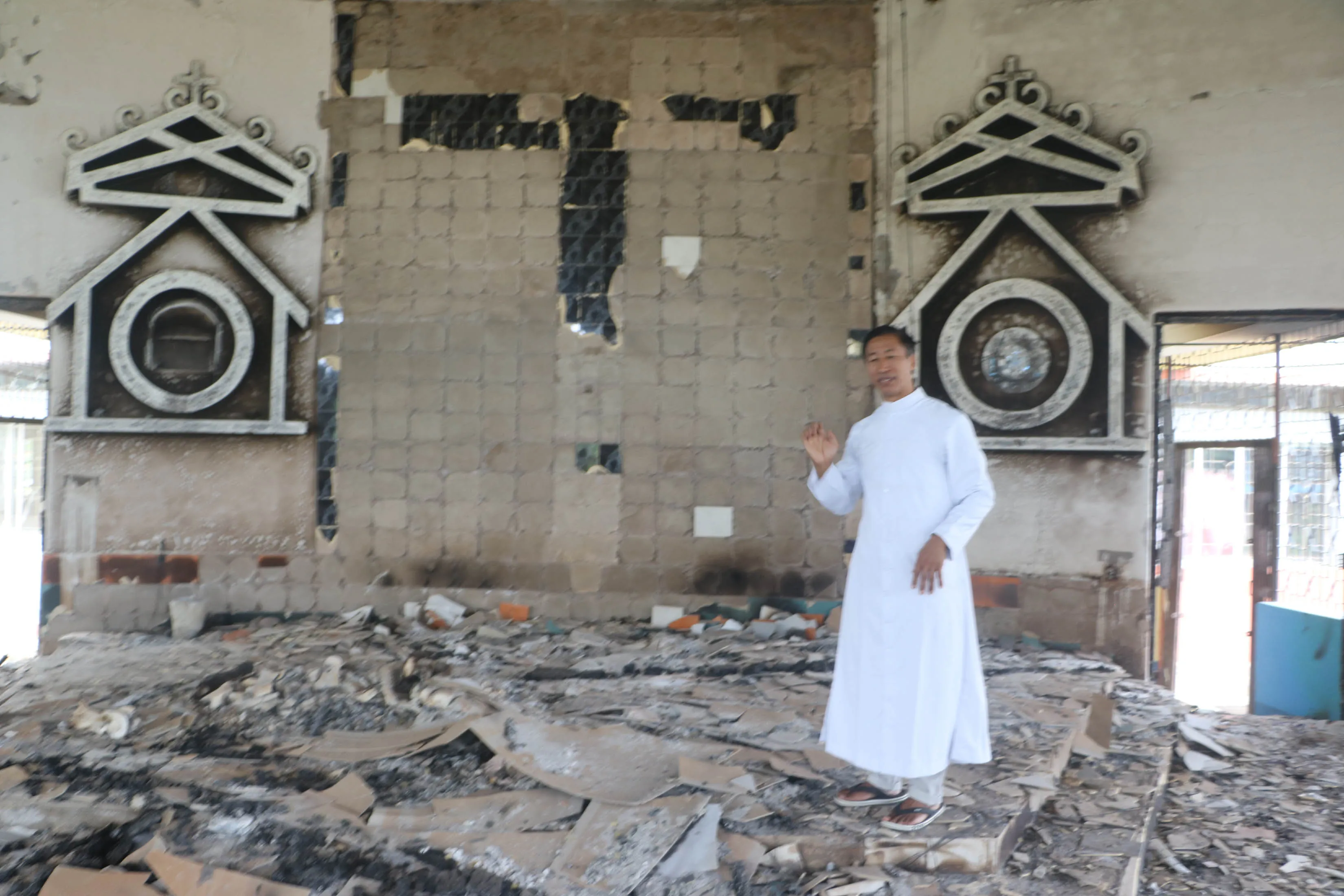 Father Isaac Honsan, pastor of St. Paul's Church, in Imphal, capital of Manipur state, stands in the rubble after the church was set on fire in a recent attack,?w=200&h=150