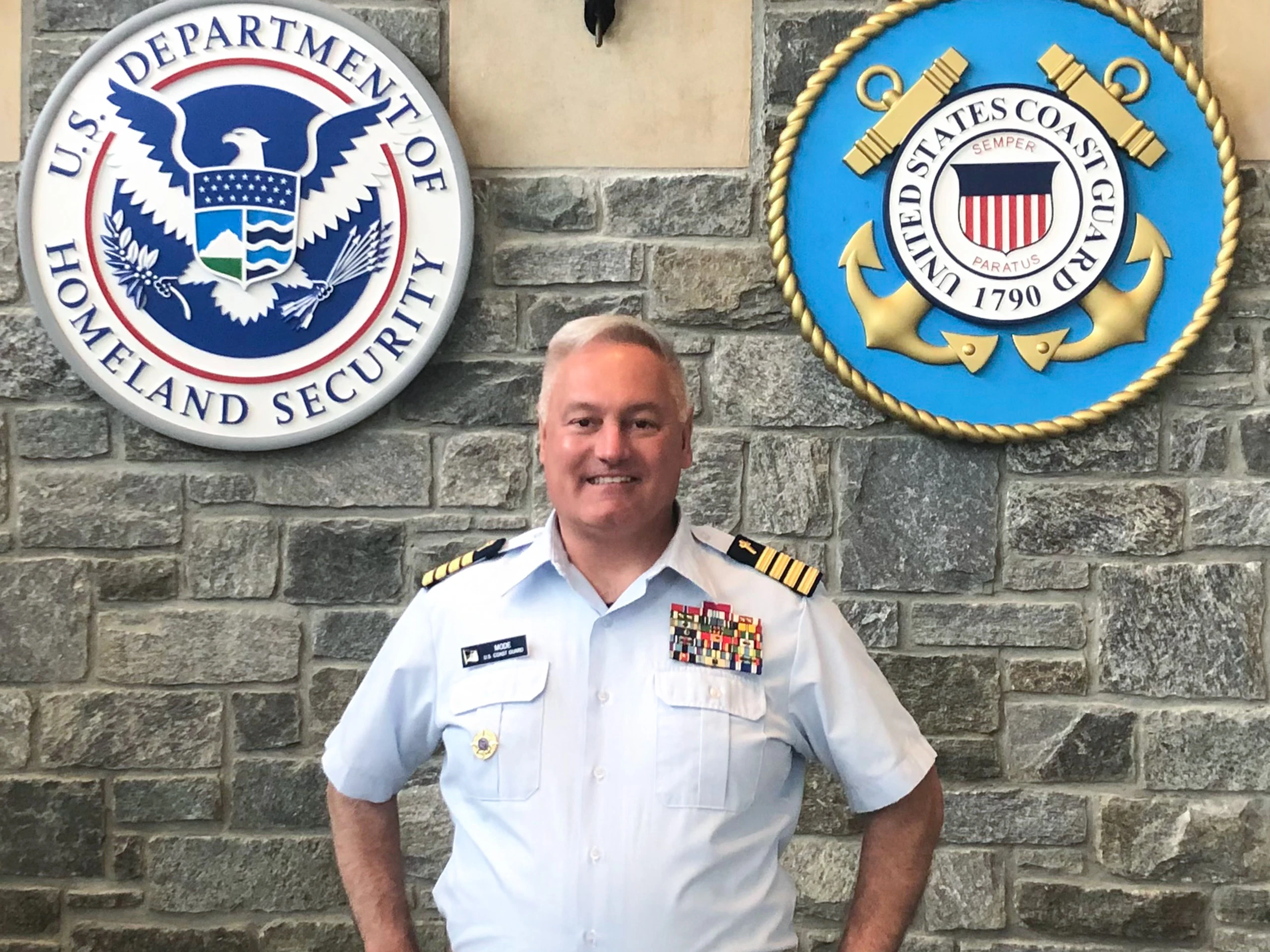 Father Daniel L. Mode, chaplain of the Coast Guard, stands in the large atrium of the Coast Guard headquarters in Washington, D.C., in front of a massive wall of flags and insignia of the Department of Homeland Security and the U.S. Coast Guard.?w=200&h=150