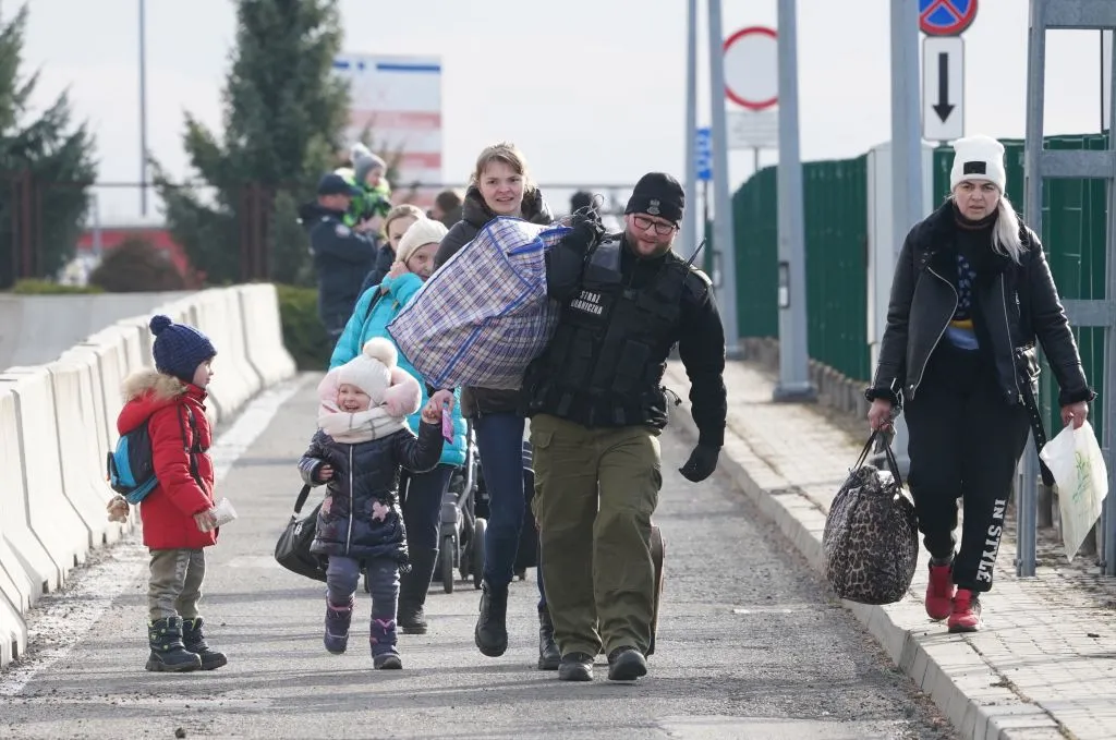 Ukrainian women with children are helped to carry their bags by a Polish border guard as Ukrainian refugees cross the border from Ukraine to Poland at the Korczowa-Krakovets border crossing, Poland, on February 26, 2022, following the Russian invasion of Ukraine.?w=200&h=150