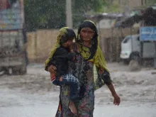 A woman carrying a child walks along a street during a heavy rainfall in the flood-hit Dera Allah Yar town in Jaffarabad district, Balochistan province, Pakistan, on Aug. 30, 2022. Aid efforts ramped up across flooded Pakistan to help tens of millions of people affected by relentless monsoon rains that have submerged a third of the country and claimed more than 1,100 lives.