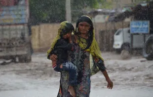 A woman carrying a child walks along a street during a heavy rainfall in the flood-hit Dera Allah Yar town in Jaffarabad district, Balochistan province, Pakistan, on Aug. 30, 2022. Aid efforts ramped up across flooded Pakistan to help tens of millions of people affected by relentless monsoon rains that have submerged a third of the country and claimed more than 1,100 lives. Photo by FIDA HUSSAIN/AFP via Getty Images