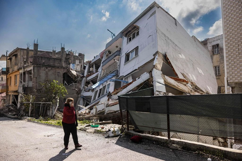 A pedestrian uses a smartphone as she walks past a collapsed building in Antakya, southern Turkey on Feb. 21, 2023. A 6.4-magnitude earthquake late Feb. 20, 2023, rocked Turkey's southern province of Hatay and northern Syria.?w=200&h=150