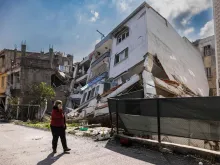 A pedestrian uses a smartphone as she walks past a collapsed building in Antakya, southern Turkey on Feb. 21, 2023. A 6.4-magnitude earthquake late Feb. 20, 2023, rocked Turkey's southern province of Hatay and northern Syria.