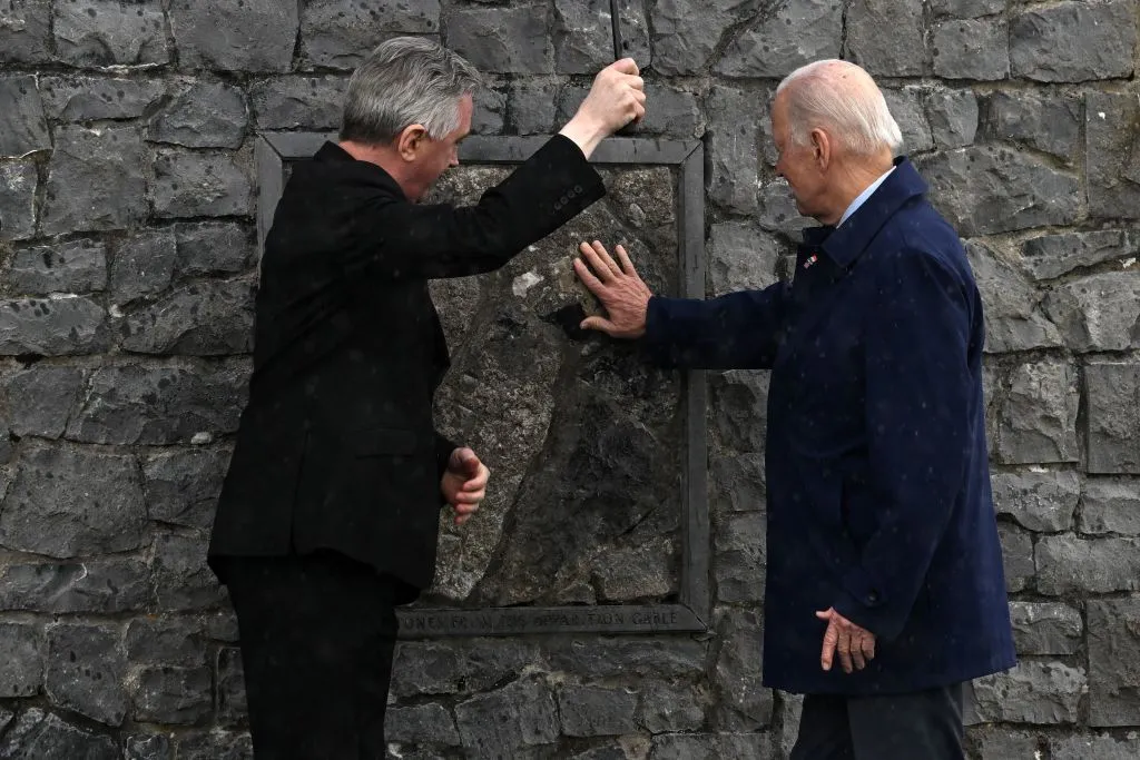 President Joe Biden and Father Richard Gibbons share an umbrella as President Biden touches the original stone from the apparition gable in the rain during a visit to Knock Shrine, on April 14, 2023, on the last day of a four-day trip to Northern Ireland and Ireland.?w=200&h=150
