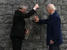 President Joe Biden and Father Richard Gibbons share an umbrella as President Biden touches the original stone from the apparition gable in the rain during a visit to Knock Shrine, on April 14, 2023, on the last day of a four-day trip to Northern Ireland and Ireland.
