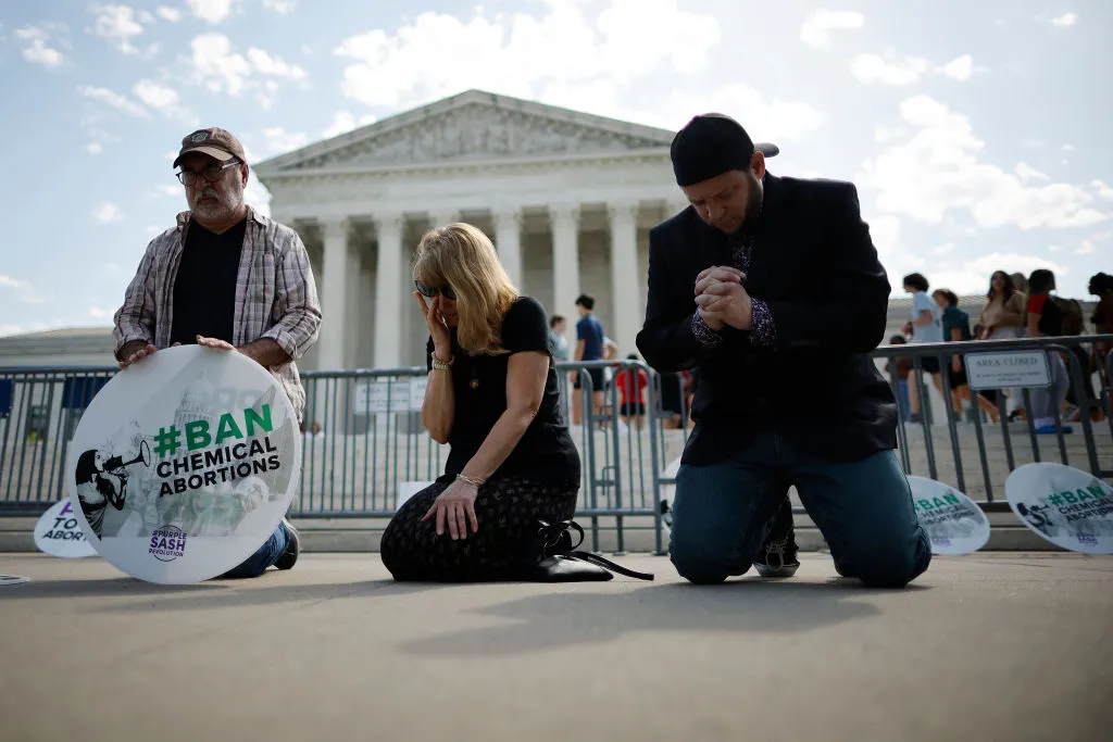 (left to right) Rev. Pat Mahoney, Peggy Nienaber of Faith and Liberty, and Mark Lee Dickson of Right to Life East Texas pray in front of the U.S. Supreme Court on April 21, 2023, in Washington, D.C. Organized by The Stanton Public Policy Center/Purple Sash Revolution, the small group of demonstrators called on the Supreme Court to affirm Federal District Court Judge Matthew Kacsmaryk’s ruling that suspends the Food and Drug Administration’s approval of the abortion pill mifepristone.?w=200&h=150