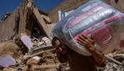 A man carries donated bedding on Sept. 13, 2023, past buildings that were ruined in the Sept. 8 earthquake in Ardouz, Morocco.