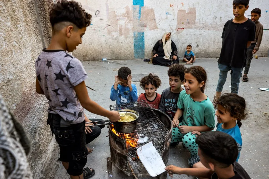 Children sit together around a boy cooking instant noodles on a fire in a makeshift oven from a recycled barrel in Rafah in the southern Gaza Strip on Oct. 31, 2023, amid ongoing battles between Israel and Hamas.?w=200&h=150
