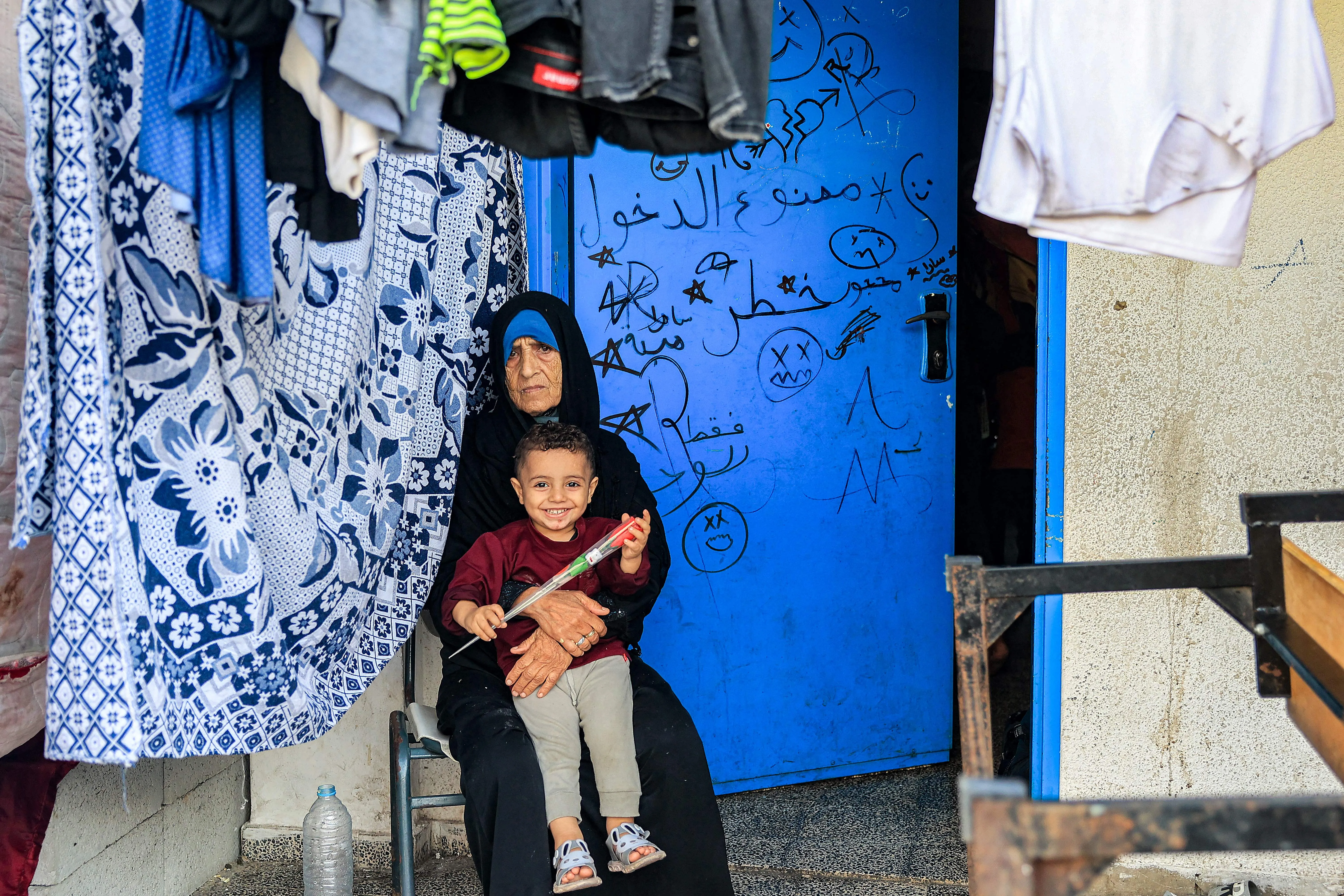 A woman sits with a child by drying laundry outside a classroom at a school run by the United Nations Relief and Works Agency for Palestine Refugees in the Near East (UNRWA) in Rafah in the southern Gaza Strip on Nov. 14, 2023, where internally displaced Palestinians have taken refuge amid ongoing battles between Israel and the Palestinian militant group Hamas.?w=200&h=150