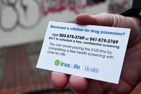 A Portland police officer holds a business card showing a number to call for a drug use health screening and services after a drug citation in order to avoid a $100 fine in downtown Portland, Oregon, on Jan. 25, 2024. Credit: PATRICK T. FALLON/AFP via Getty Images