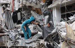 A Palestinian woman assists a child playing on the ruinas of a building destroyed by earlier Israeli bombardment in Gaza City on April 8, 2024, amid the ongoing conflict between Israel and the Palestinian Hamas militant group. Credit: AFP via Getty Images