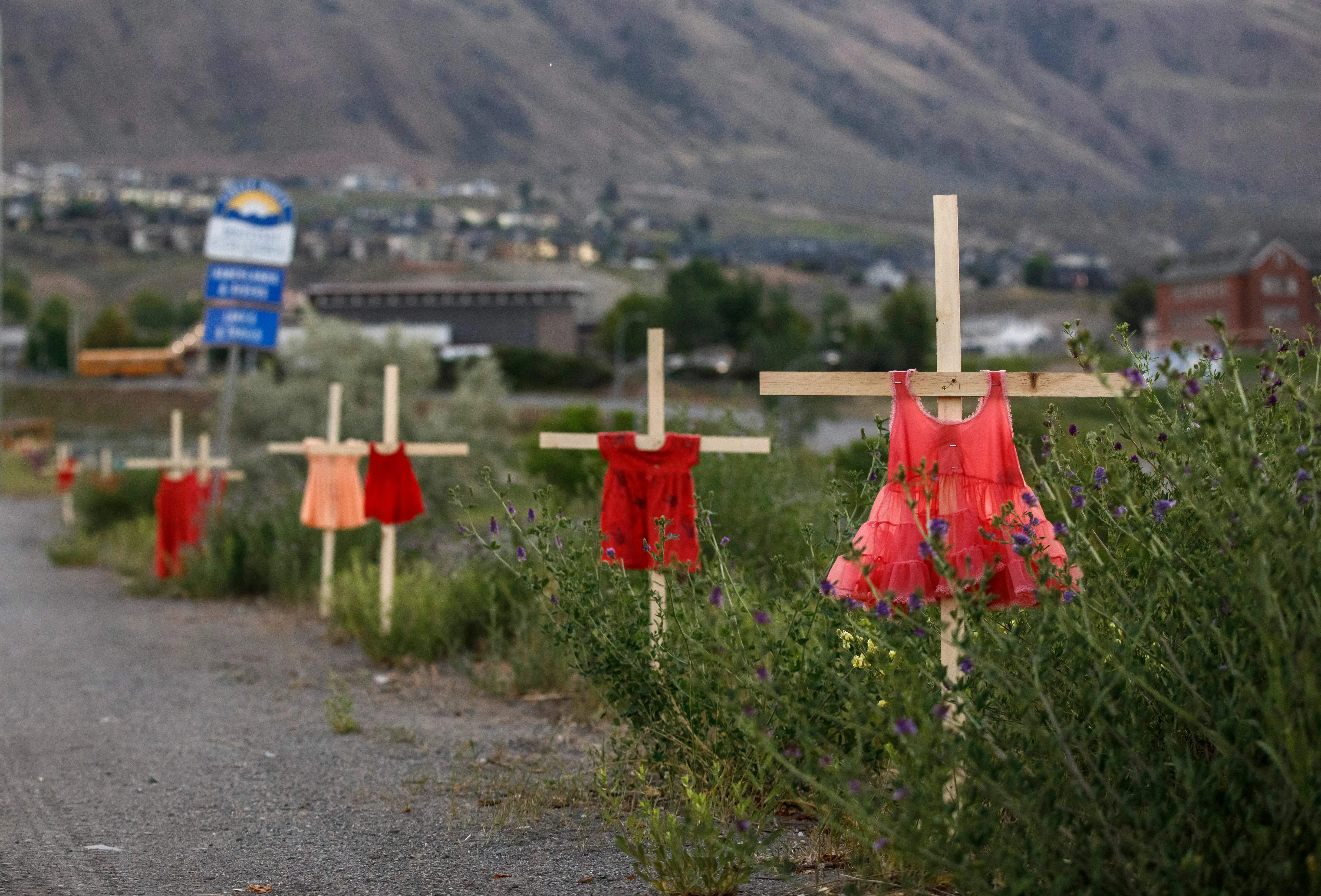 Children's red dresses are staked along a highway near the former Kamloops Indian Residential School where flowers and cards have been left as part of a makeshift memorial created in response to media reports that the "remains" of 215 children have been discovered buried near the facility, in Kamloops, British Columbia, Canada, on June 2, 2021.?w=200&h=150