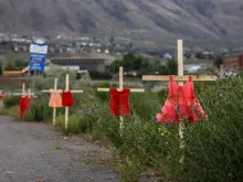 Children's red dresses are staked along a highway near the former Kamloops Indian Residential School where flowers and cards have been left as part of a makeshift memorial created in response to media reports that the "remains" of 215 children have been discovered buried near the facility, in Kamloops, British Columbia, Canada, on June 2, 2021.