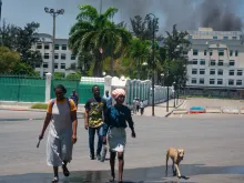 As smoke billows from the Ministry of Finance building behind them, people leave the area after hearing gunshots from armed gangs near the National Palace in Port-au-Prince, Haiti, on April 2, 2024.