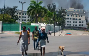 As smoke billows from the Ministry of Finance building behind them, people leave the area after hearing gunshots from armed gangs near the National Palace in Port-au-Prince, Haiti, on April 2, 2024. Credit: CLARENS SIFFROY/AFP via Getty Images