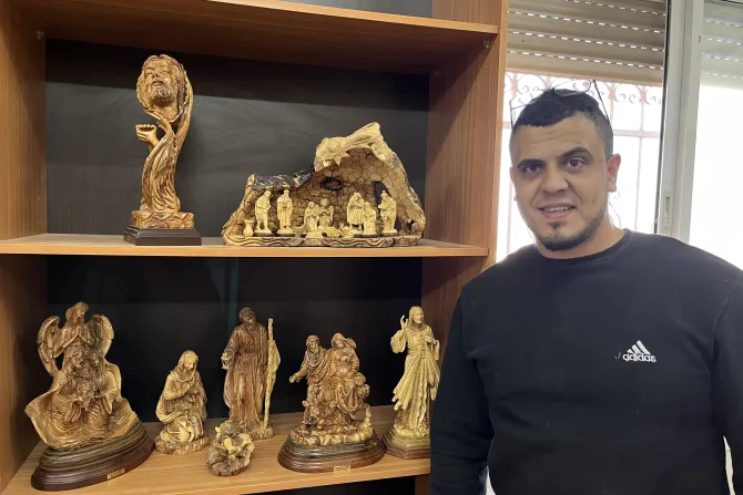 Alber Zakharia standing beside wooden figurines that he personally carved.