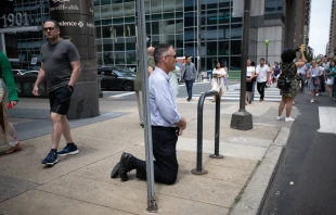 A man kneels as the National Eucharistic Procession passes by in Philadelphia on May 30, 2024. Credit: Jeffrey Bruno