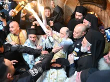 The Greek Orthodox Patriarch Theophilos III exits the Aedicule of the Holy Sepulcher on May 4, 2024, in Jerusalem, showing the faithful the two candles just lit from the oil lamp that is believed to have been miraculously ignited inside Jesus' tomb.