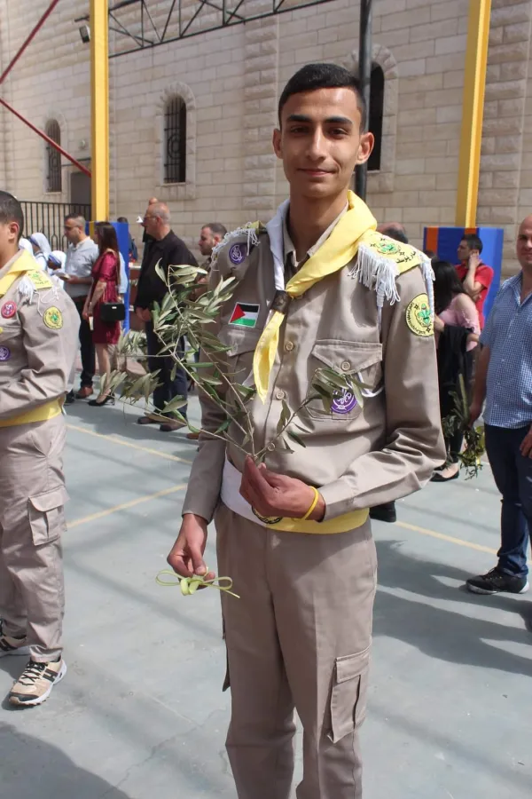 Suhail Abu Dawod, in a scout uniform, holds an olive branch in one hand and a palm leaf woven into a cross in the other. The photo is from Palm Sunday 2023. Today Abu Dawod says: "We beseech God for peace, the same peace spread throughout the world at the time of Jesus’ resurrection. My fervent prayers are dedicated to justice and the establishment of lasting peace in the Holy Land, particularly in our city of Gaza." Credit: Courtesy of Father Gabriel Romanelli