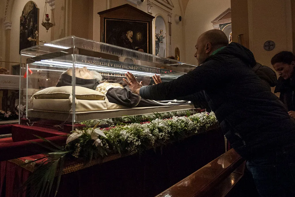 A man places his hands on the glass urn holding the remains of St. Pio in Pietrelcina, Italy, in 2016. St. Pio was found to be in a state of partial deterioration and partial preservation when his coffin was opened in 2008, but experts present at the exhumation have said there was no supernatural quality to what was preserved. Artificial preservation techniques have since been applied to conserve his body from further deterioration and a lifelike mask has been placed over his skull.?w=200&h=150