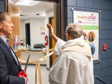 A priest blesses the new integrated pediatric clinic, one of the first of its kind to be based out of a shelter for families experiencing homelessness in the country, April 20, 2023, before the ceremonial ribbon cutting by Darren Walsh, president & CEO of Catholic Charities of Denver.