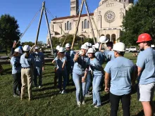 A group of volunteers stand in front of a Notre-Dame Cathedral truss replica at the Catholic University of America in Washington, D.C., on Sept. 26, 2022.