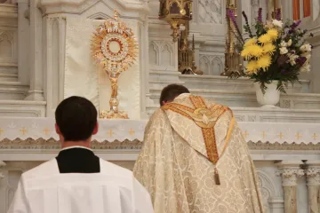 A priest bows before the Eucharist, housed in a gold monstrance.