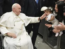 Pope Francis, seated in a wheelchair, greets a child during the pope's general audience at the Vatican on Jan. 25, 2023.